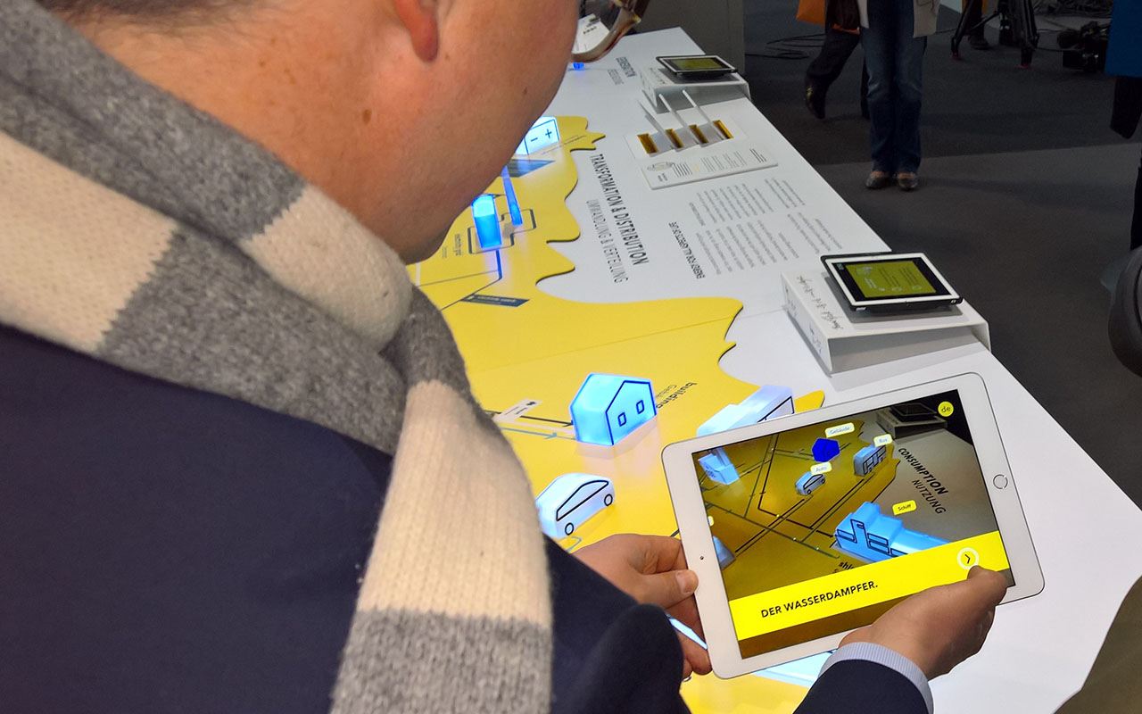 Ein Besucher hält ein Tablet über ein Ausstellungsmodell