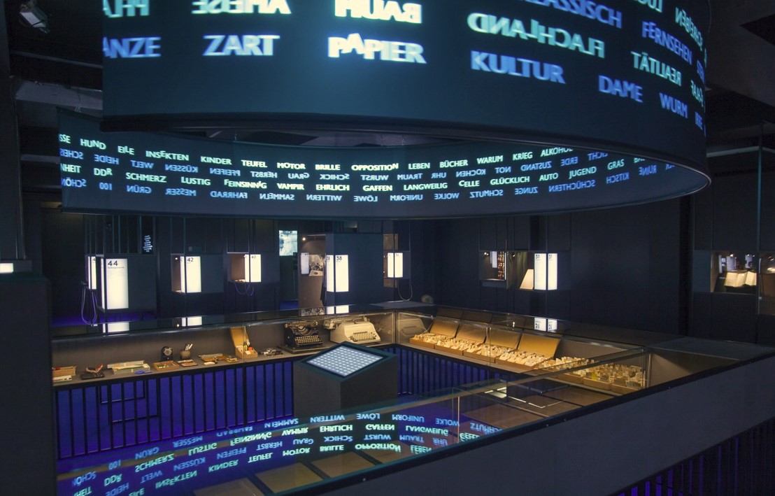 Umlaufende Schriftprojektion mit Wörtern über einem Ausstellungsraum mit Vitrinen
