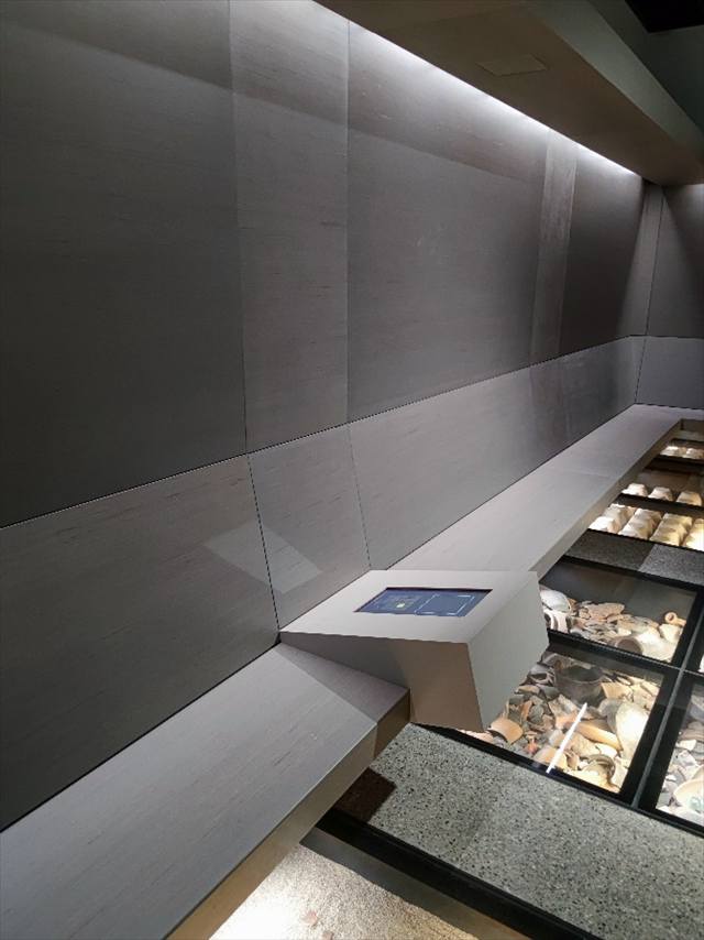 Ausstellungsnische mit Touchscreen-Pult an einer Sitzbank und Bodenvitrinen mit Funden