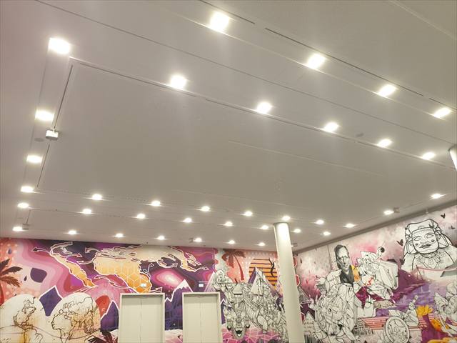 Weiße Decke mit Einbauleuchten und kleinen Lautsprechern über einer farbigen Wandillustration
