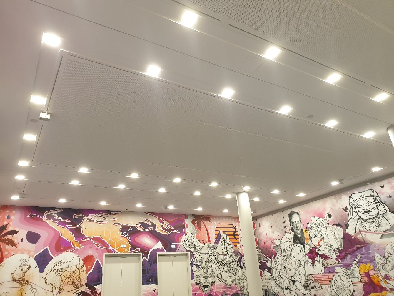 Weiße Decke mit Einbauleuchten und kleinen Lautsprechern über einer farbigen Wandillustration