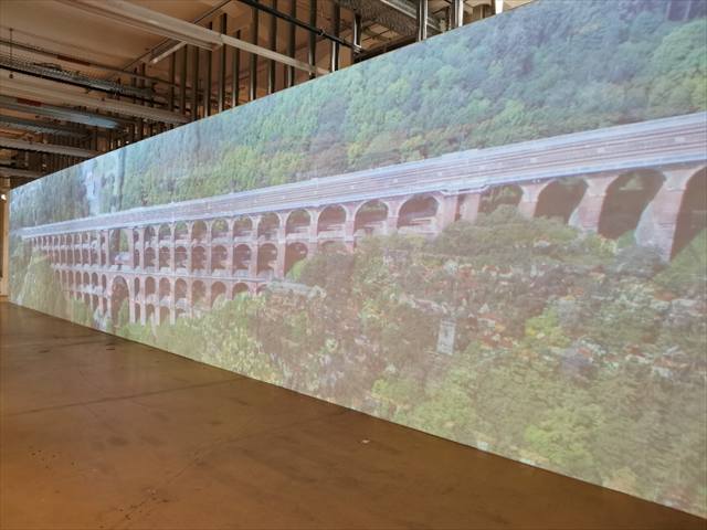 Großflächige Wandprojektion eines Eisenbahnviadukts in einer Industriehalle