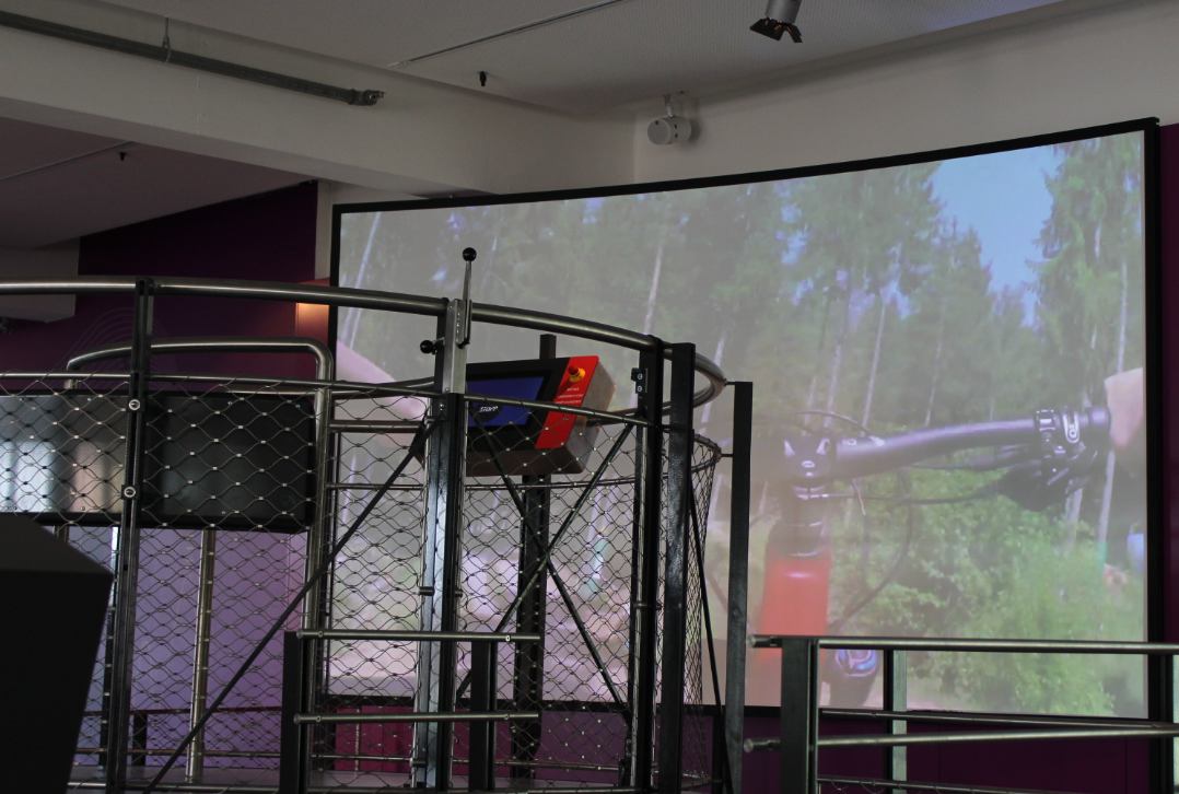 Station in einem Metallgestell vor einer großen, gebogenen Projektionsfläche mit Waldmotiv