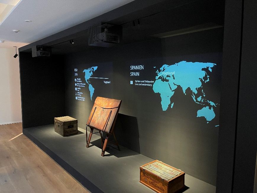 Projektion einer Weltkarte hinter historischen Transportkisten und einem Holzgestell auf einem Podest