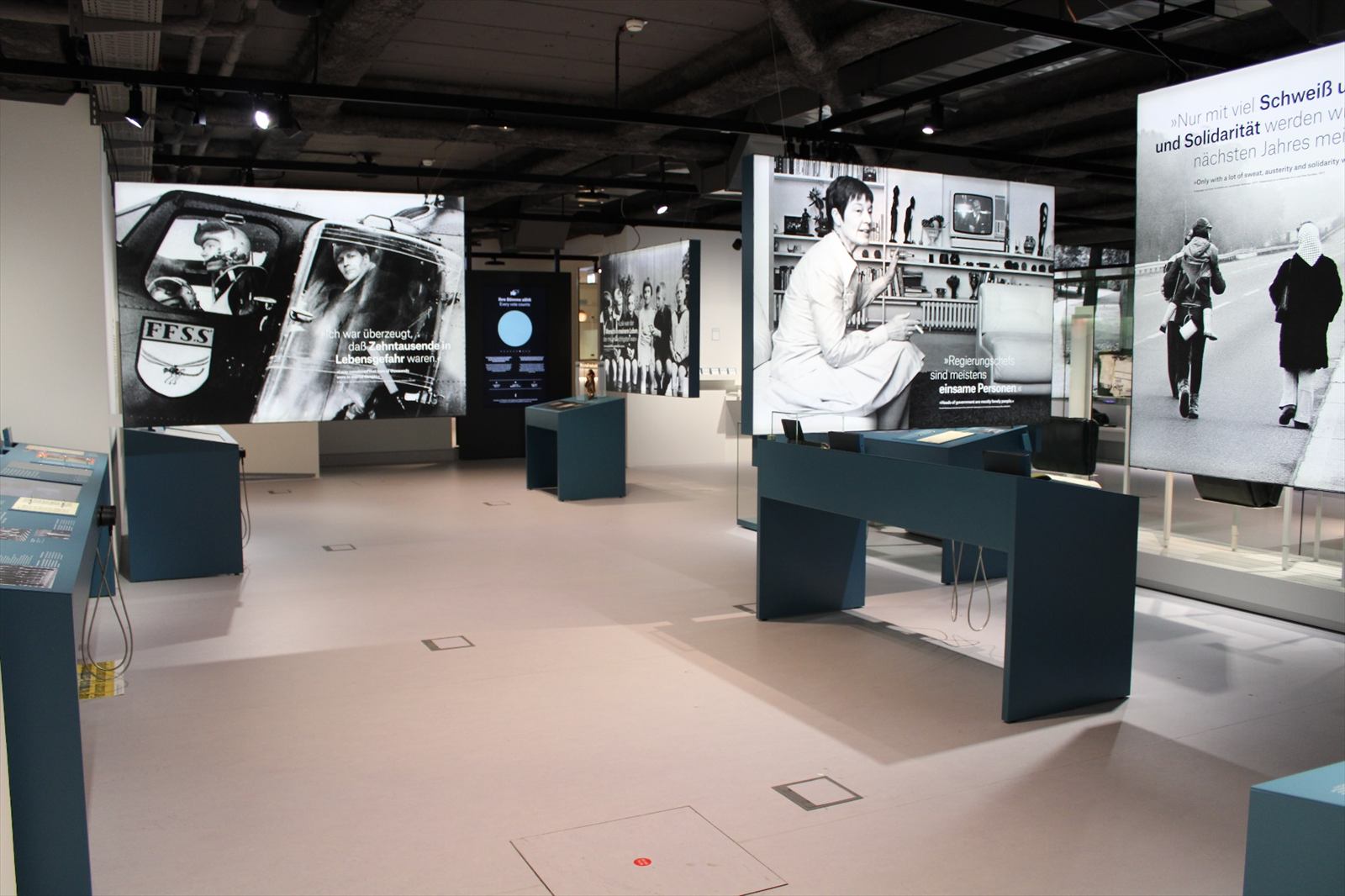 Ausstellungsraum mit großformatigen Schwarz-Weiß-Fotos und petrolfarbenen Medientischen