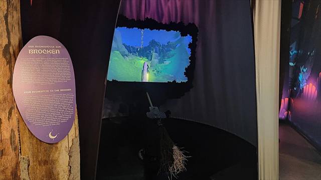 Virtueller Flug über eine Berglandschaft auf einer Bildfläche, davor ein montierter Hexenbesen