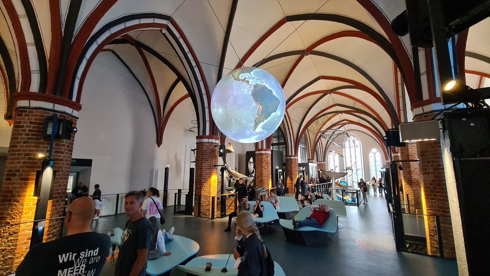 Kirchenhalle mit großem, schwebendem Projektionsglobus über Sitzbereichen und Besuchern