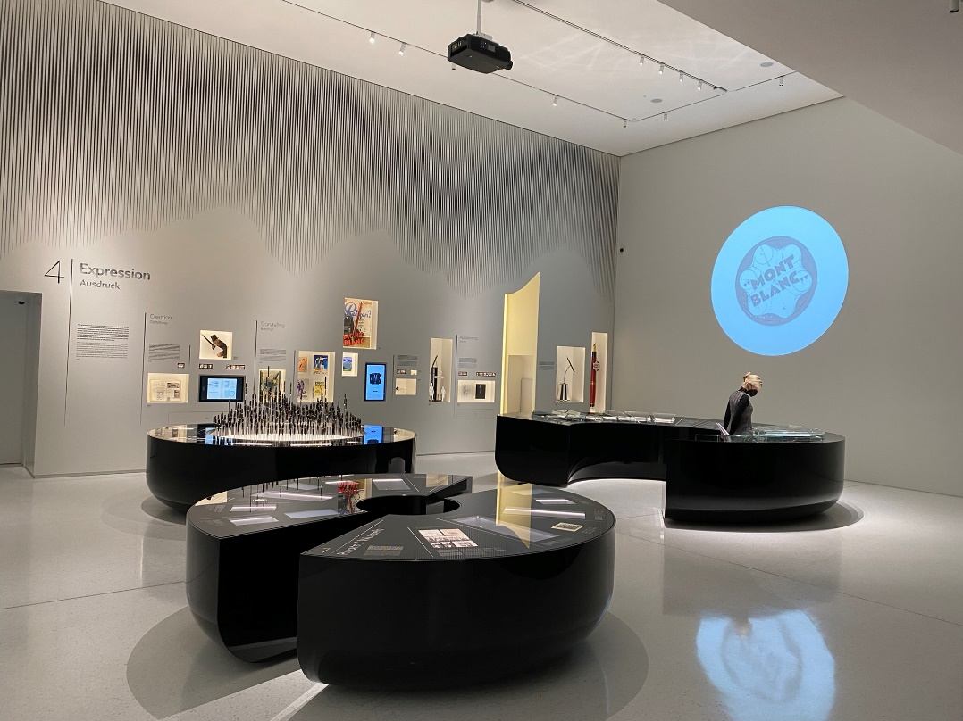 Ausstellungsraum mit runden Vitrinentischen, Wandexponaten und Projektion