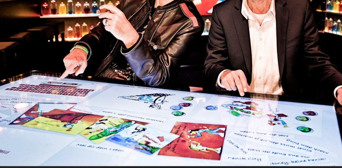 Hände auf einem beleuchteten Multitouch-Tisch mit farbigen Bildmotiven