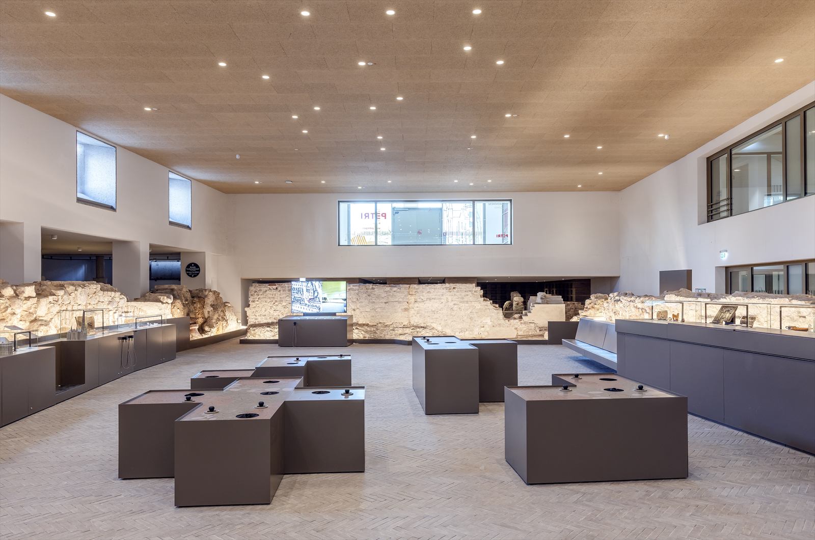 Ausstellungshalle mit kubischen Ausstellungsmöbeln und freigelegten Fundamenten entlang der Wände