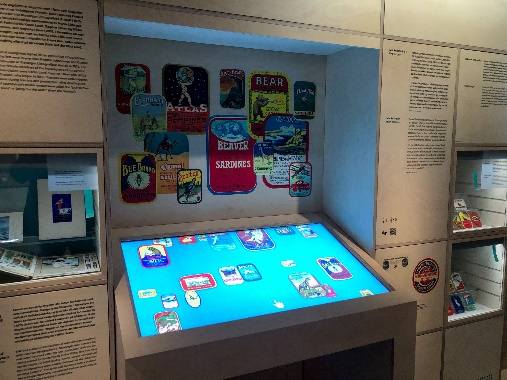 Multitouch-Tisch mit digitalen Konservendosen-Etiketten vor einer Wand mit historischen Etiketten