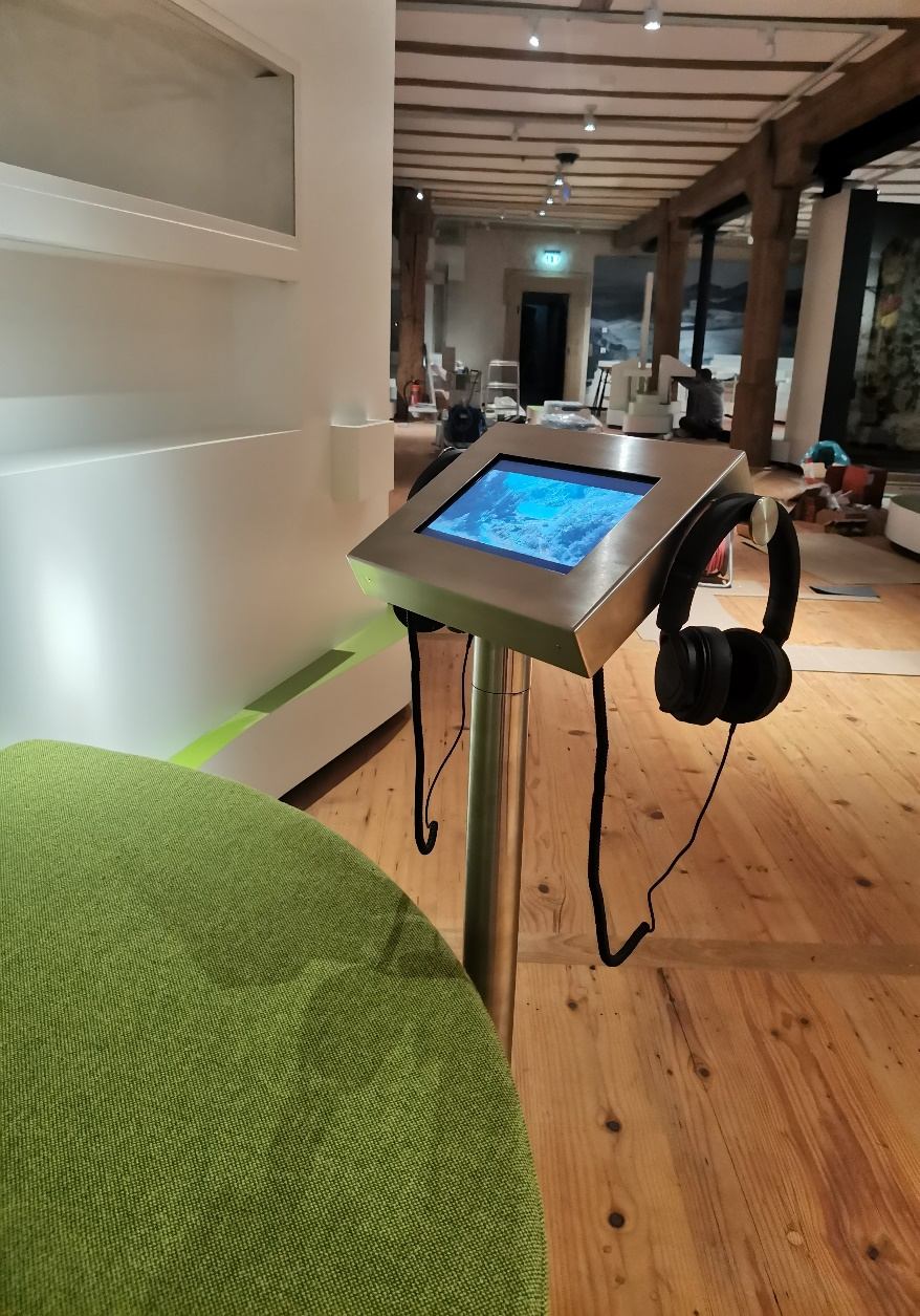 Touchscreen-Pult mit Kopfhörern im Ausstellungsraum mit Holzboden und Holzbalkendecke