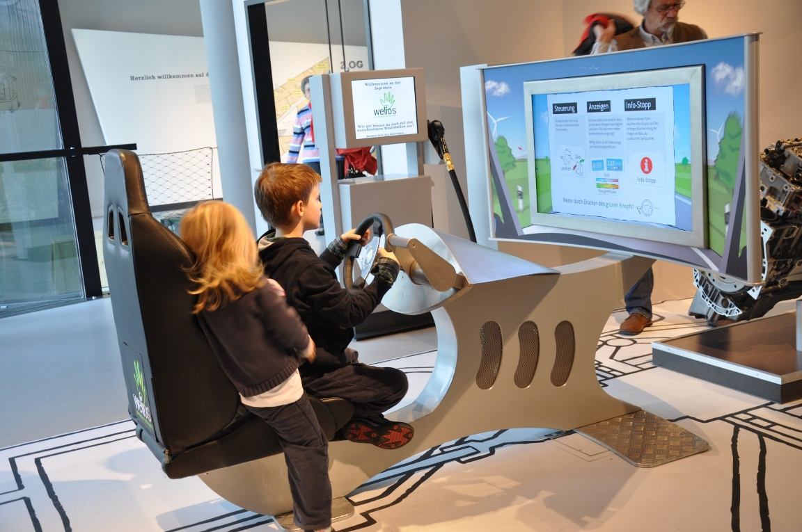 Kinder im Fahrsimulator mit Lenkrad vor großem Bildschirm