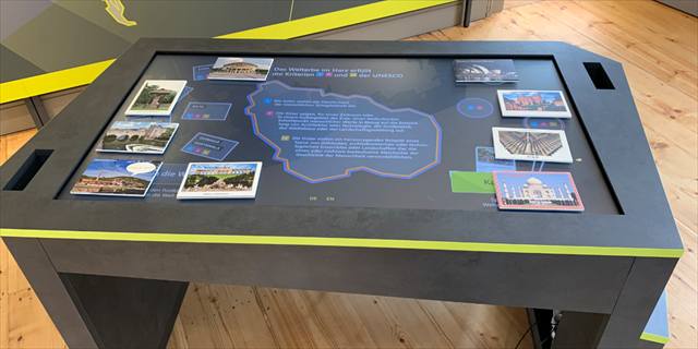 Multitouch-Tisch mit Bildkarten von Welterbestätten rund um eine Harz-Grafik
