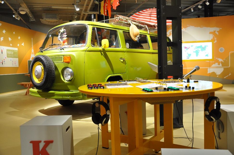Ausstellungsbereich mit grünem VW-Bus und rundem Tisch mit Kopfhörern und Mikrofon